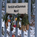 Ein Schild am Stahltor. Auf dem Schild steht "Herzlich willkommen Mark!". Das Schild ist dekoriert mit Fichtenzweigen, Zapfen und Äpfeln.