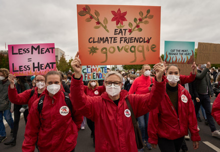 Group of people at a protest with signs saying "Less Meat = Less Heat", "Eat climate friendly, #GoVeggie" and "Cut the meat, lose the heat"
