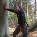 A tree cutter is standing next to a tree with his left hand leaning on the tree.