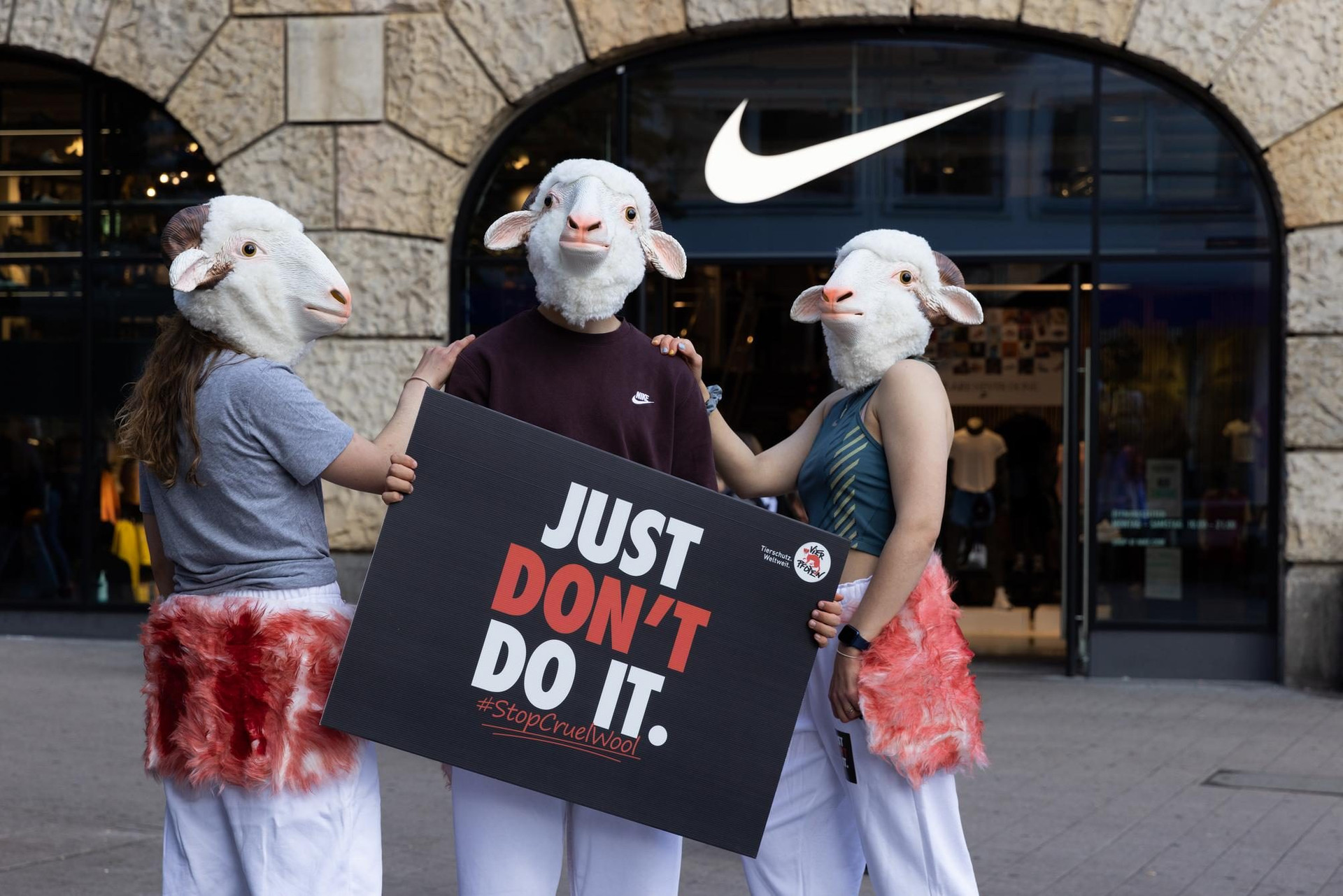 Protesters wearing sheep masks outside a Nike store with a placard saying "Just don't do it: #StopCruelWool".